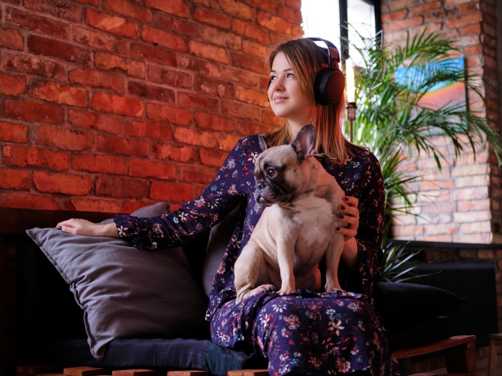 happy blonde woman dress sitting with her cute pug handmade sofa listening music room with loft interior